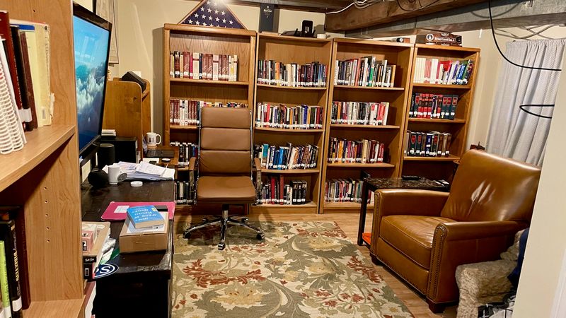 A home office library setting with wooden bookshelves filled with books, a desk with a computer monitor, and classroom environment during the COVID-19 era