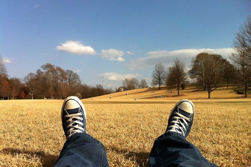 Person relaxing on a grassy field wearing Converse sneakers on an autumn day